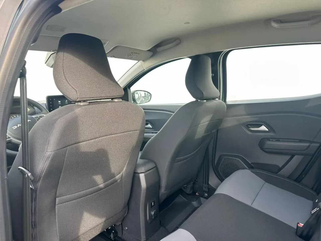 Vue intérieure arrière de la Dacia Sandero III Stepway 2025, sièges tissu noir et gris, console centrale visible.