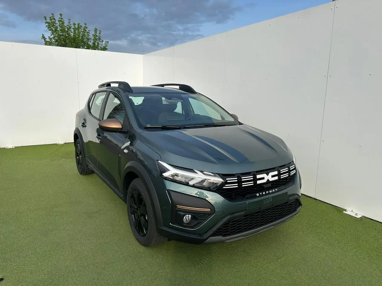 Vue 3/4 avant droit d'une Dacia Sandero III Stepway 2025 vert cèdre avec détails brun cuivré et jantes noires.