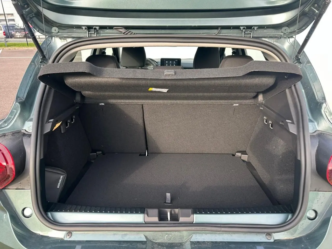 Coffre ouvert vu de l'arrière d'une Dacia Sandero III Stepway 2025 vert cèdre, intérieur noir et tablette de coffre relevée.
