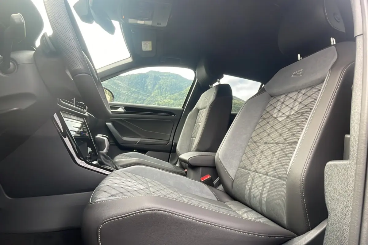 Vue intérieure côté droit montrant les sièges avant en tissu et cuir gris avec surpiqûres et accoudoir central du Volkswagen T-Roc.