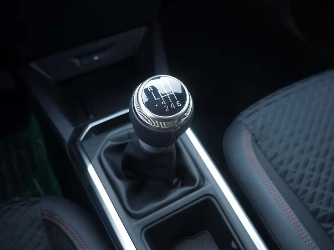 Gros plan sur le levier de vitesses manuel de la Renault Clio VI bleu iron, avec sellerie noire et surpiqûres rouges.