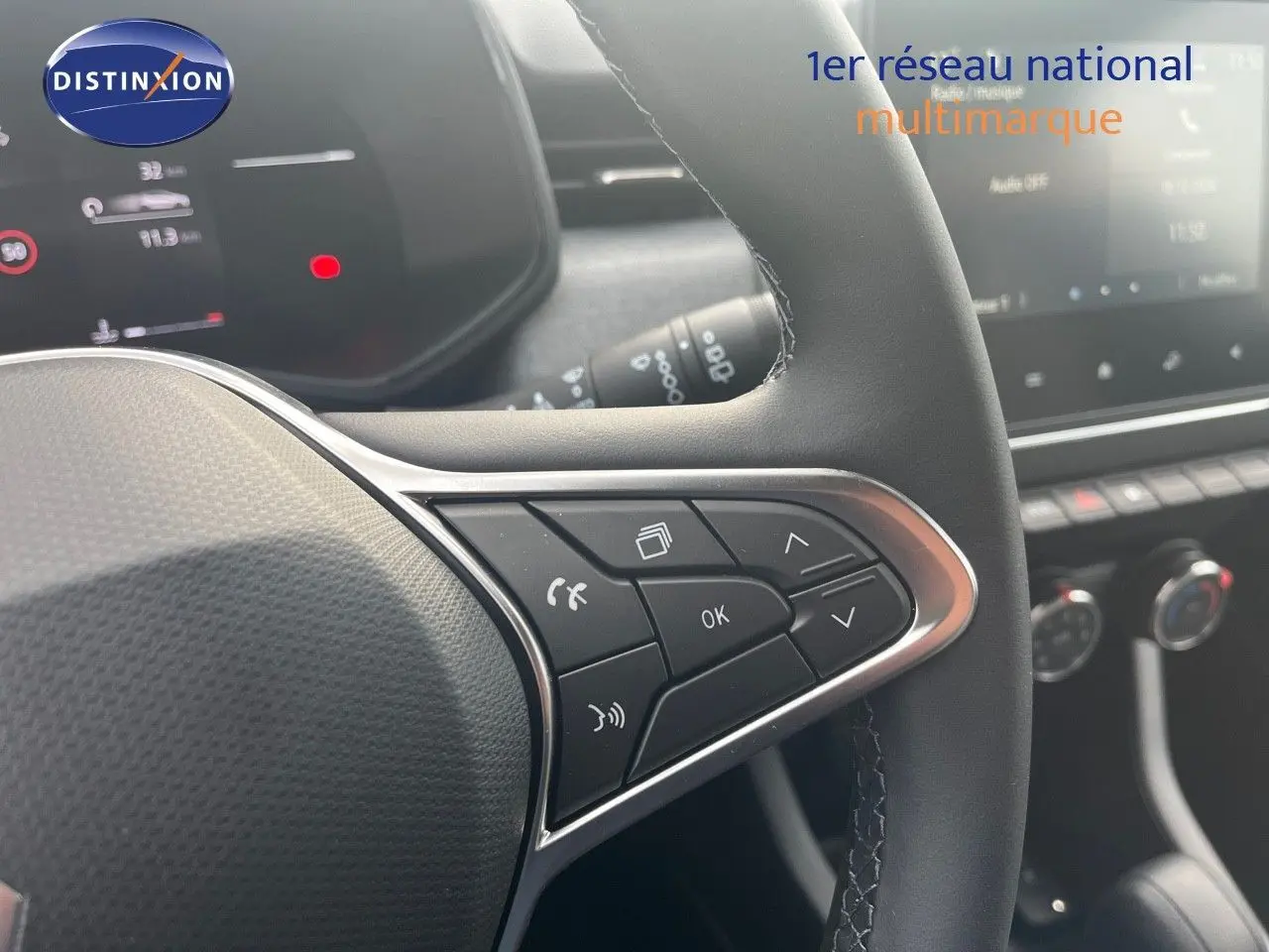 Gros plan sur les commandes au volant côté gauche d'une Renault Clio gris schiste métal, tableau de bord numérique en arrière-plan.