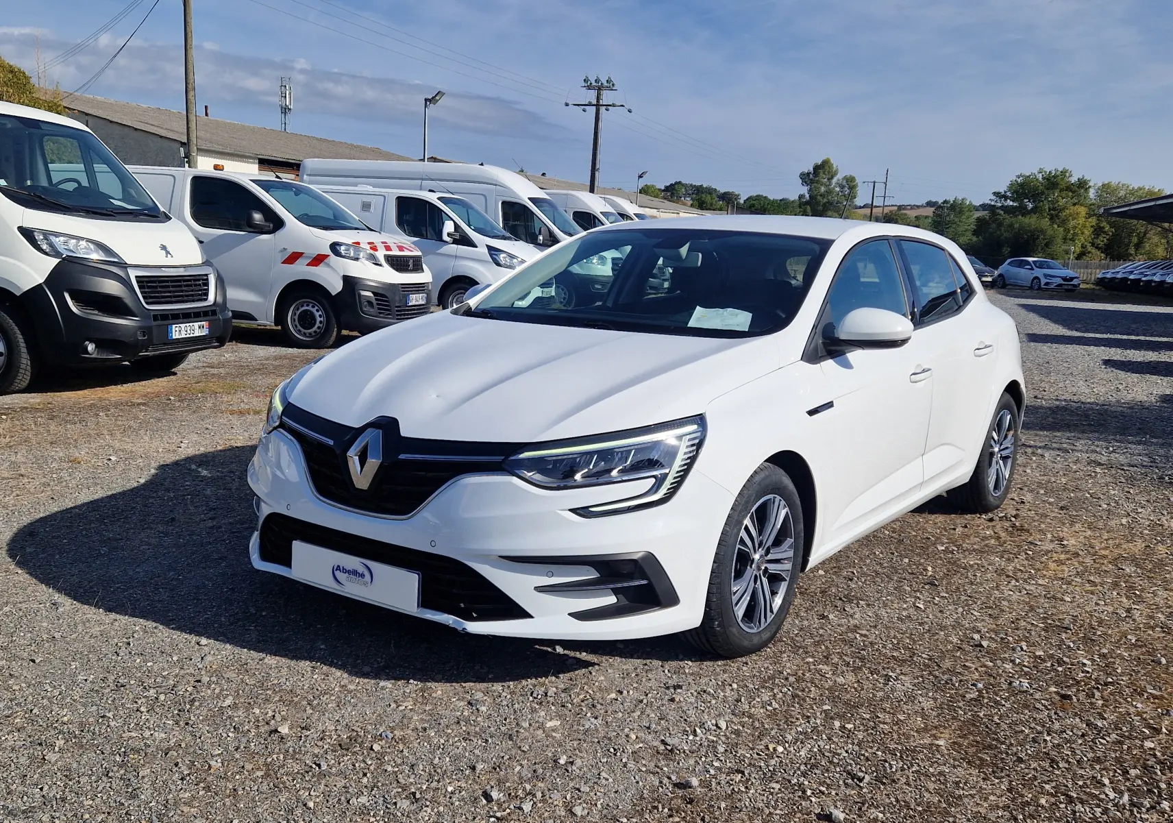 Renault Mégane 1.5 Blue dCi 115 Evolution blanche vue 3/4 avant droit sur parking ensoleillé.