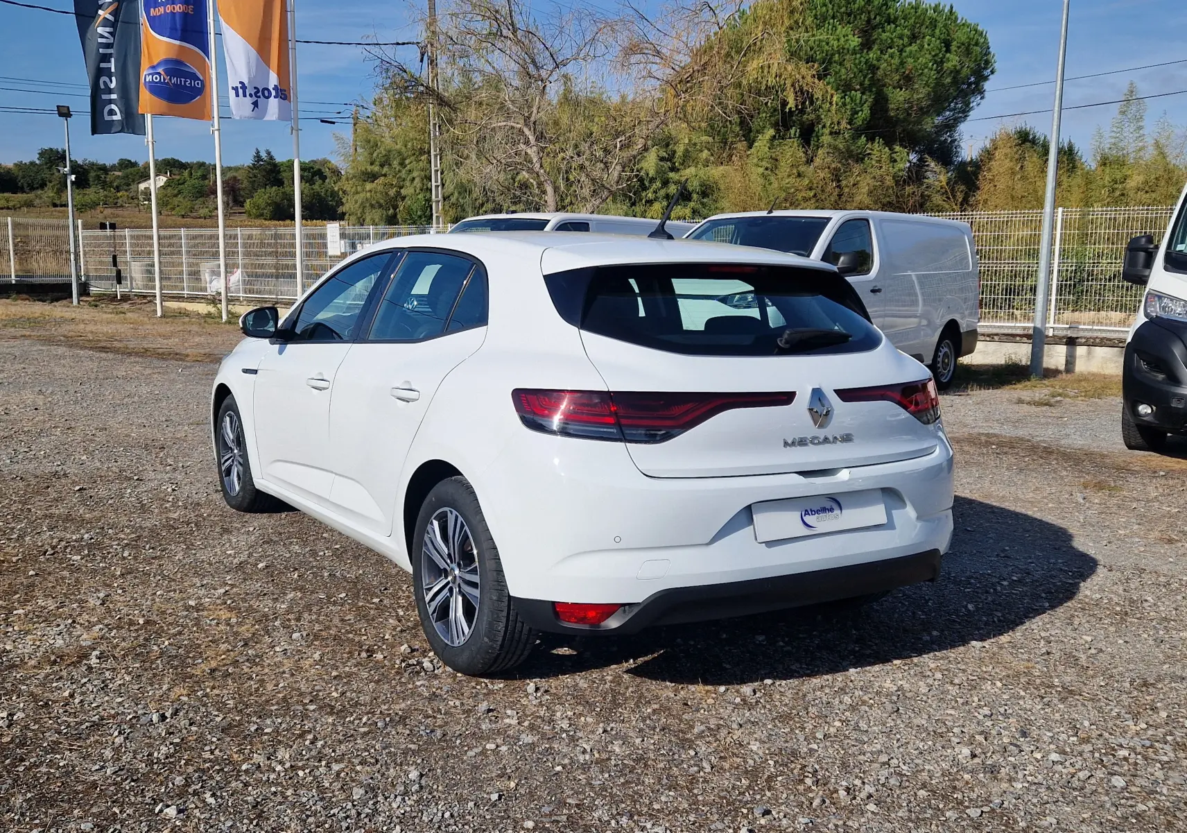 Renault Mégane blanche vue 3/4 arrière droit sur parking, avec feux arrière LED et jantes alliage 16 pouces.