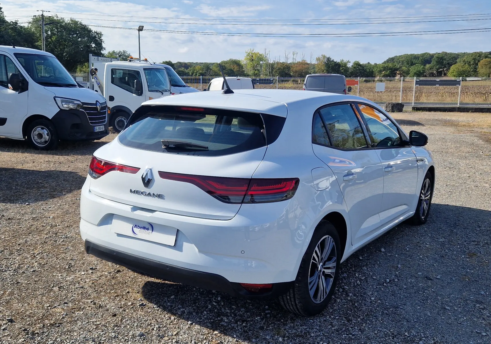 Renault Mégane blanche vue 3/4 arrière droit sur un parking, avec feux arrière LED et jantes alliage.