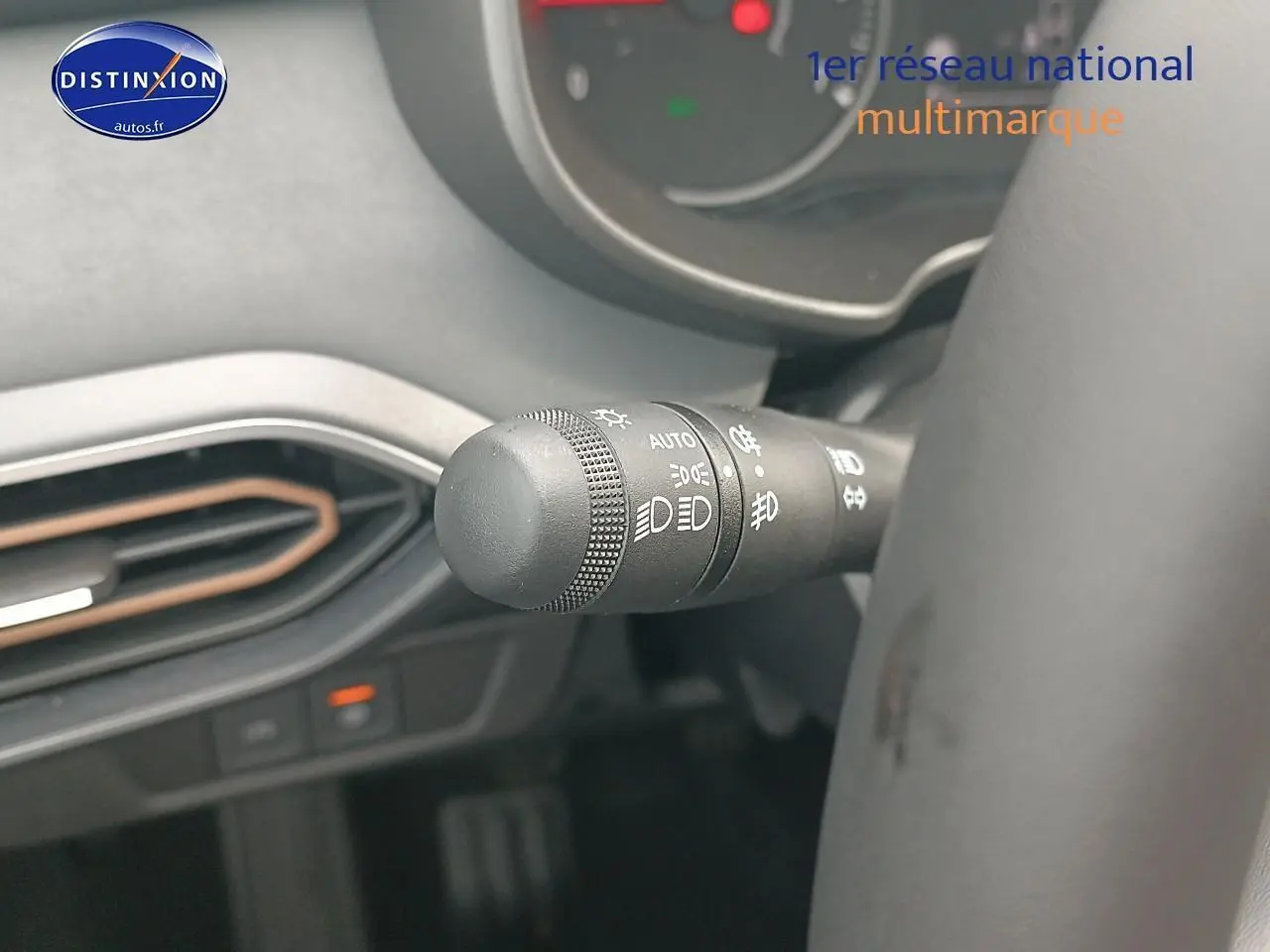 Gros plan sur la commande des phares à gauche du volant dans l'habitacle noir de la Dacia Sandero 2025.