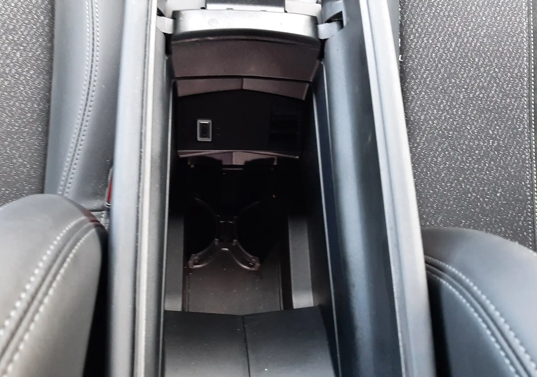 Vue plongeante sur le rangement central noir entre les sièges avant d'une Peugeot 308 SW 2024, finition cuir gris.