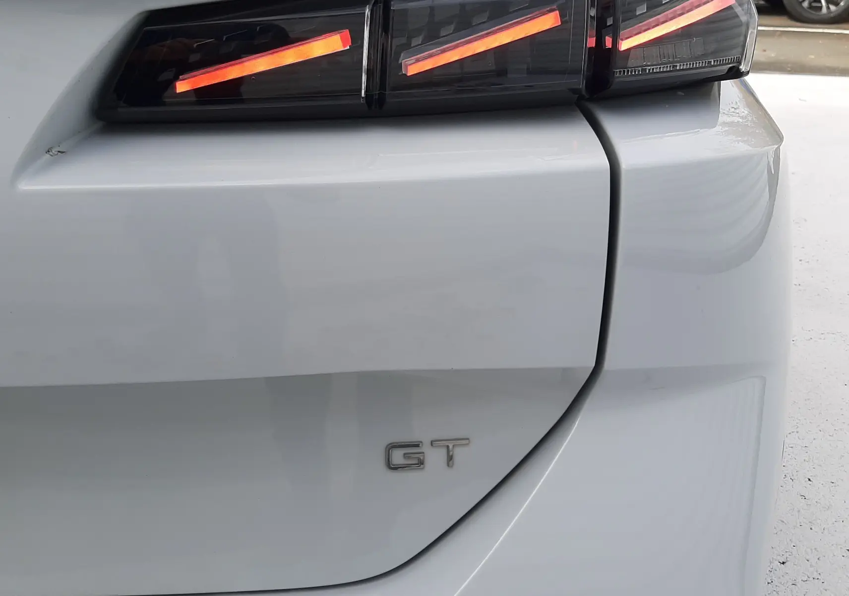 Gros plan sur le feu arrière droit allumé et le badge GT d'une Peugeot 308 SW blanche Okenite de 2024.