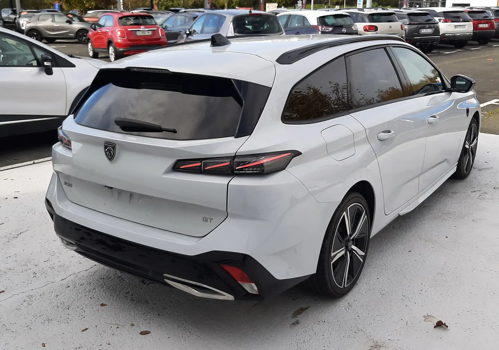 Vue 3/4 arrière droite d’une Peugeot 308 SW blanche Okenite avec vitres teintées et feux arrière LED distinctifs.