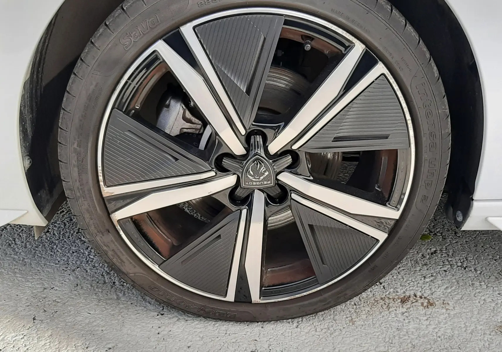 Gros plan sur la roue avant droite d’une Peugeot 308 SW blanche, avec jante alliage noire et argentée au design moderne.