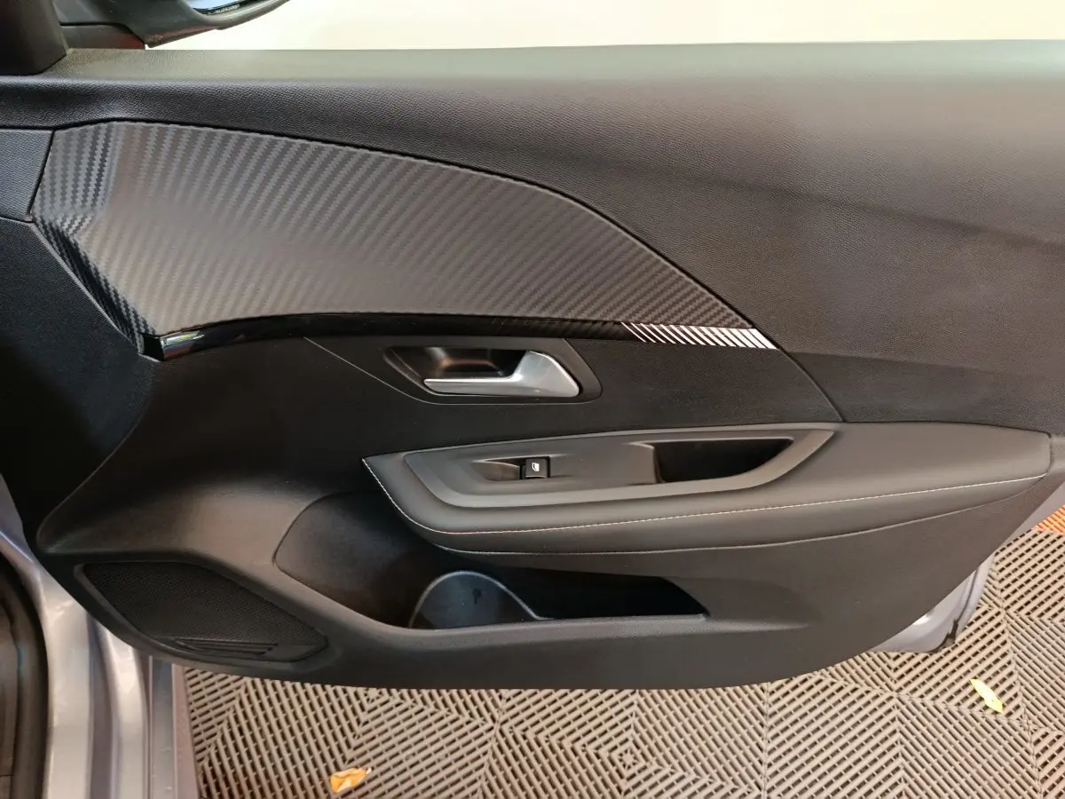 Vue côté gauche de la porte intérieure noire avec insert effet carbone d'une Peugeot 208 gris clair 2025 PureTech Allure