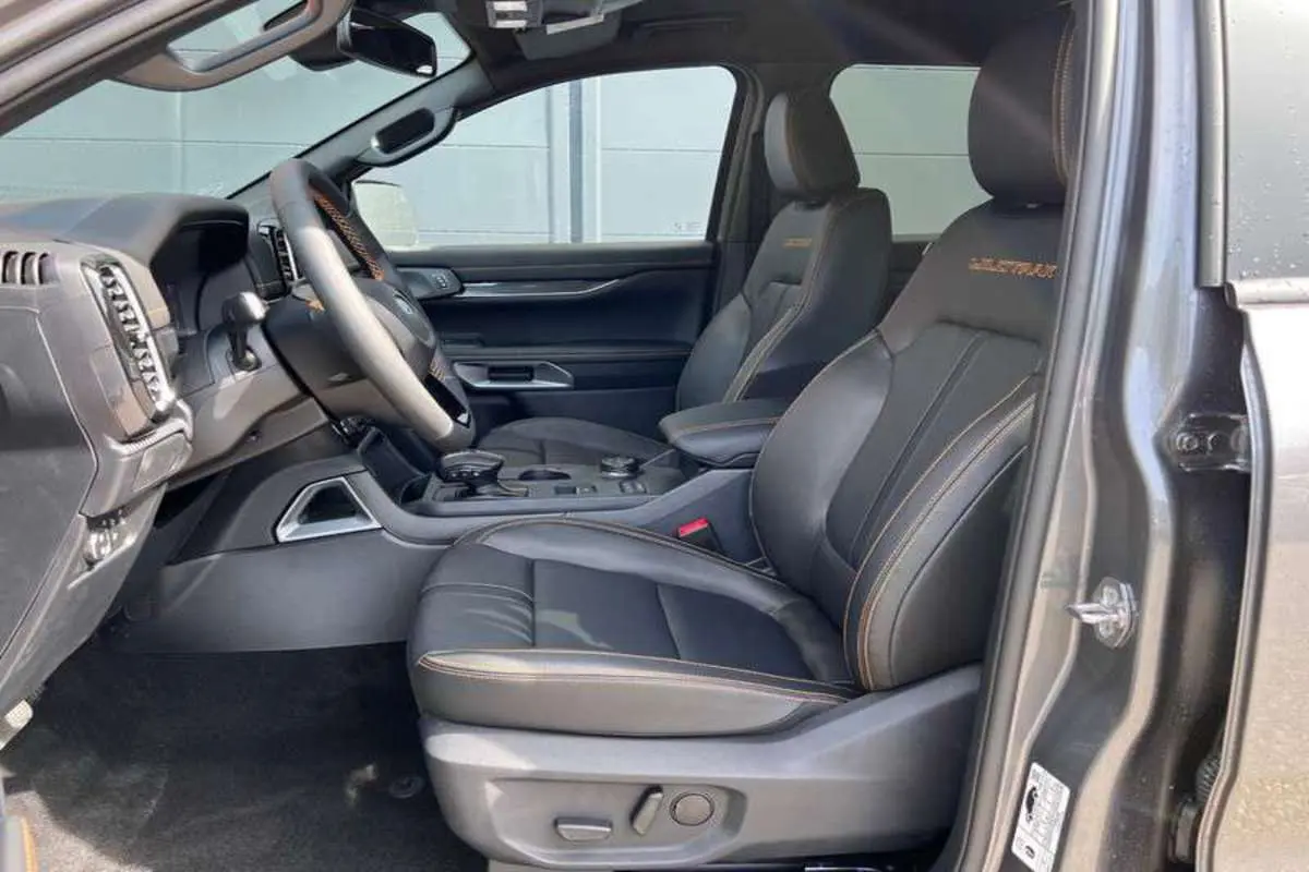 Vue intérieure côté conducteur du Ford Ranger Wildtrak Plus 2025, sièges cuir noirs avec surpiqûres orange et logo brodé.