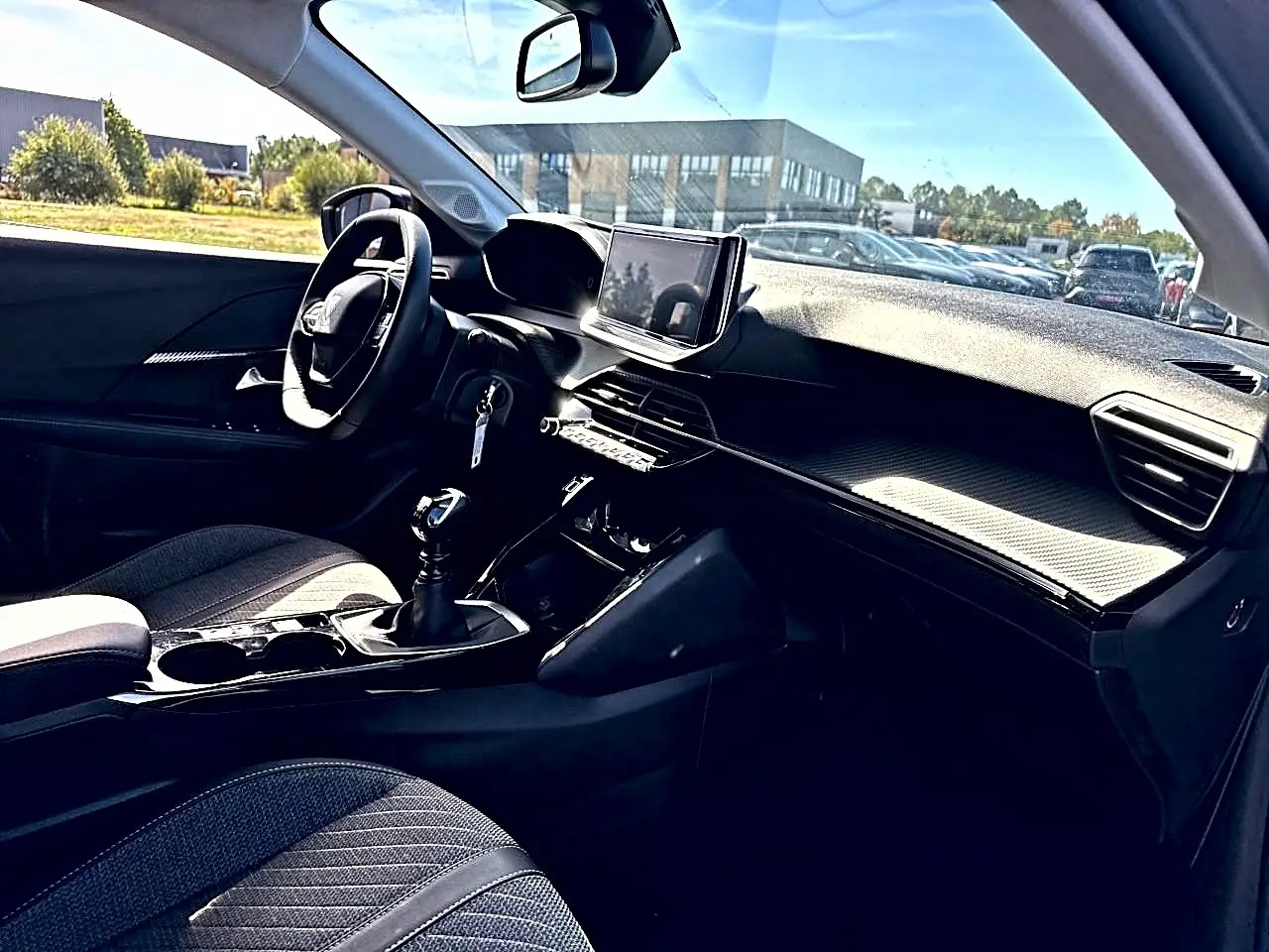 Vue intérieure côté conducteur de la Peugeot 208 1.2 100 Allure avec volant, écran tactile et sellerie tissu gris.