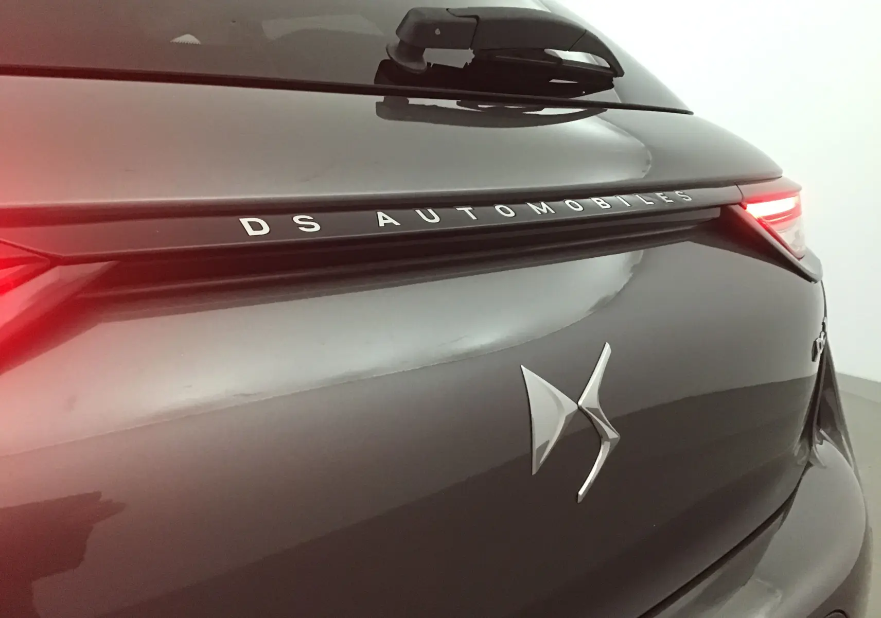 Gros plan sur l'arrière droit gris platinium du DS3 Crossback 2024 avec feux allumés et logo DS Automobiles visible.