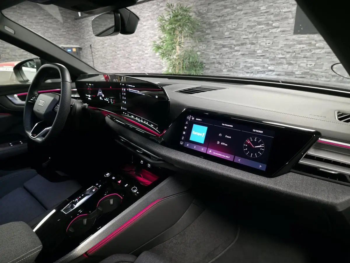 Intérieur Audi A5 Avant 2025 vu côté conducteur, tableau de bord noir avec éclairage d'ambiance rose et double écran tactile.