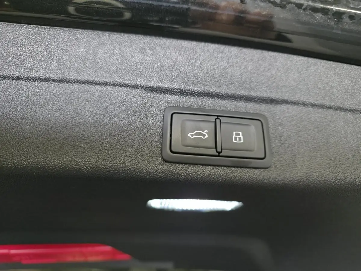 Boutons d'ouverture de hayon et de verrouillage intégrés sur le panneau intérieur du coffre d'une Audi A5 Avant noire.