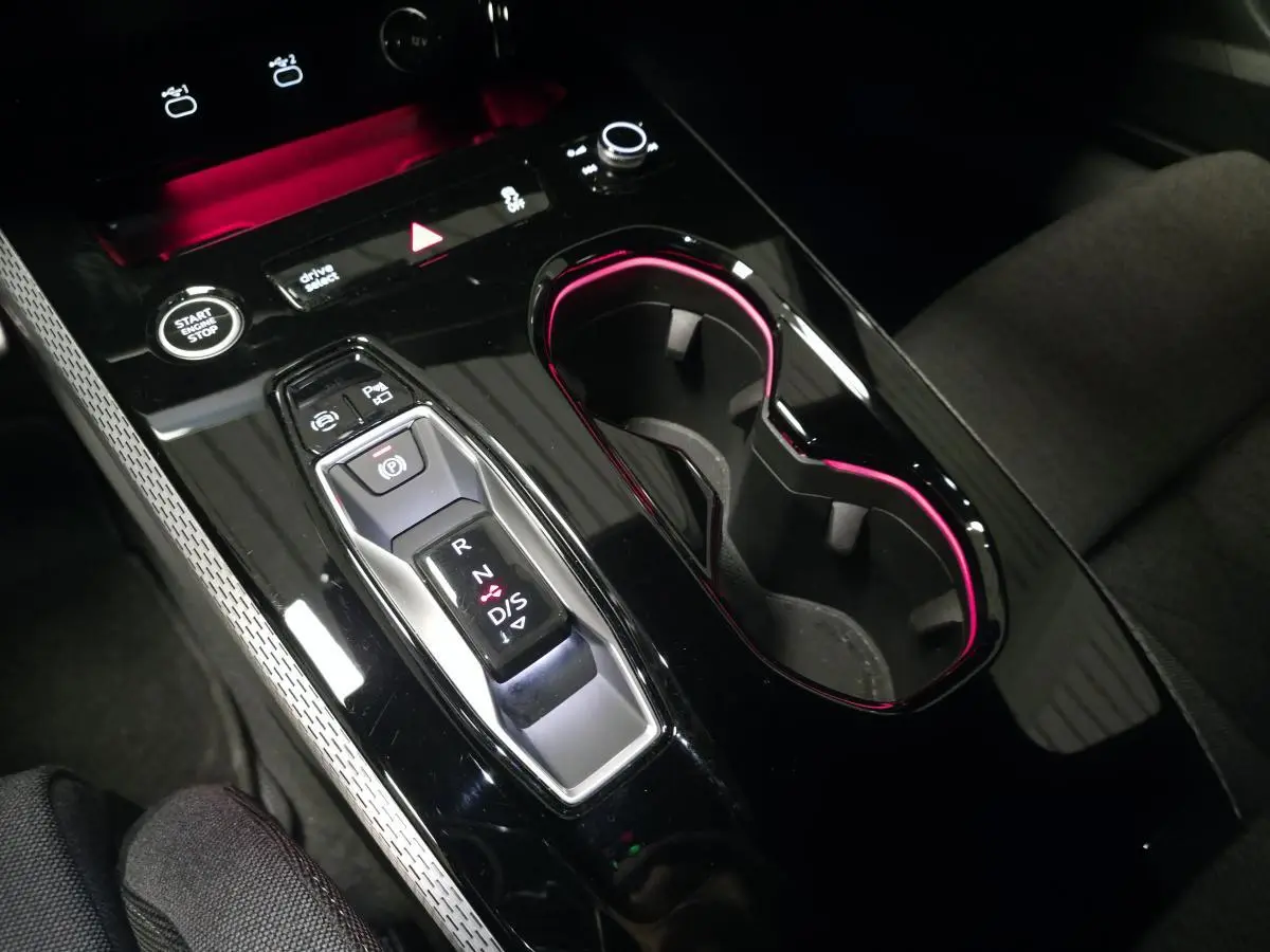 Gros plan sur la console centrale noire brillante de l'Audi A5 Avant 2025 avec éclairage d'ambiance rose autour des porte-gobelets.