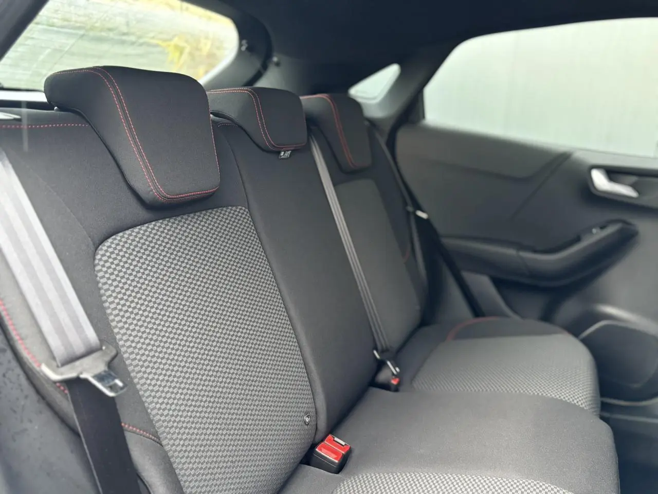 Vue intérieure du siège arrière droit du Ford Puma 2024, tissu gris avec surpiqûres rouges et ceintures de sécurité.