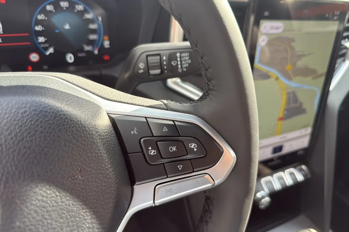 Gros plan sur le volant cuir multifonctions noir du Volkswagen Amarok 2026 avec écran tactile de navigation visible.