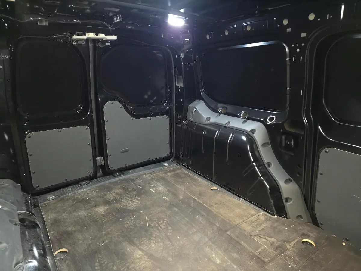Vue intérieure arrière du Volkswagen Caddy Cargo noir 2024, montrant l'espace de chargement avec plancher en bois et parois renforcées.