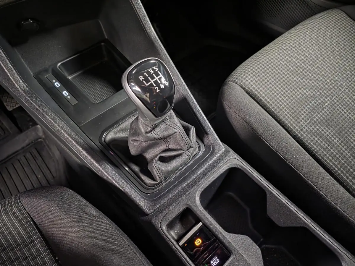 Vue rapprochée de la console centrale du Volkswagen Caddy 2024 noire, avec levier de vitesses manuel et frein à main électrique.