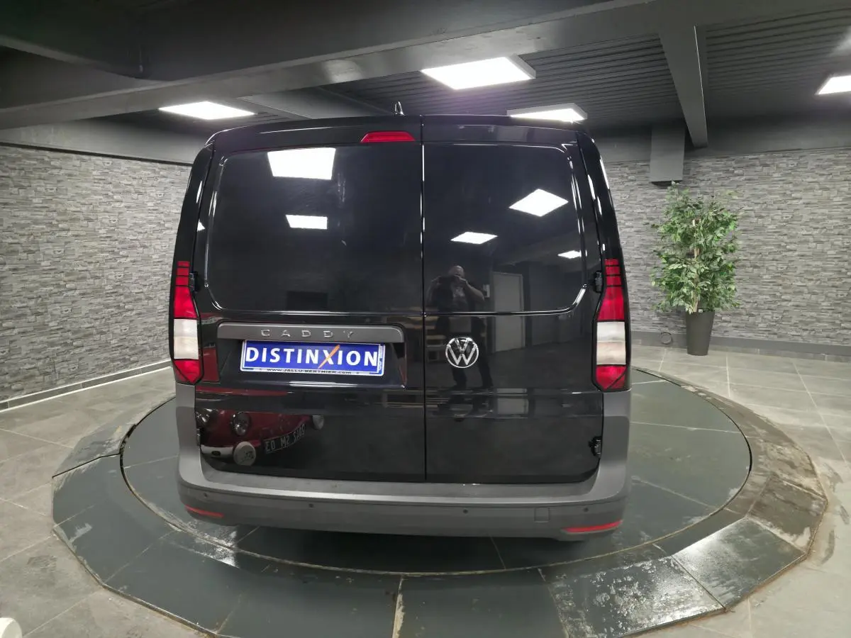 Vue arrière d'un Volkswagen Caddy Cargo noir avec portes battantes et pare-chocs gris dans un showroom.