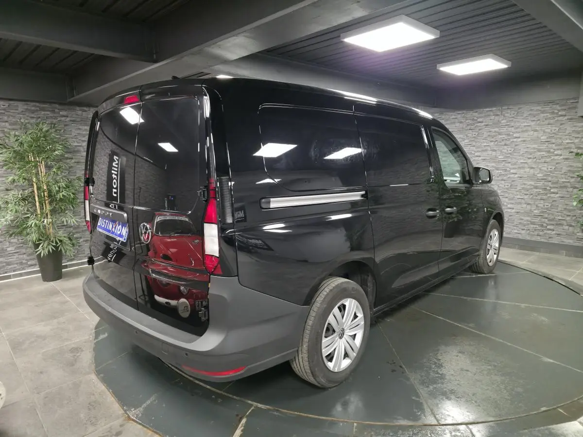 Vue 3/4 arrière droite d’un Volkswagen Caddy Cargo noir métallisé avec portes arrière battantes dans un showroom.