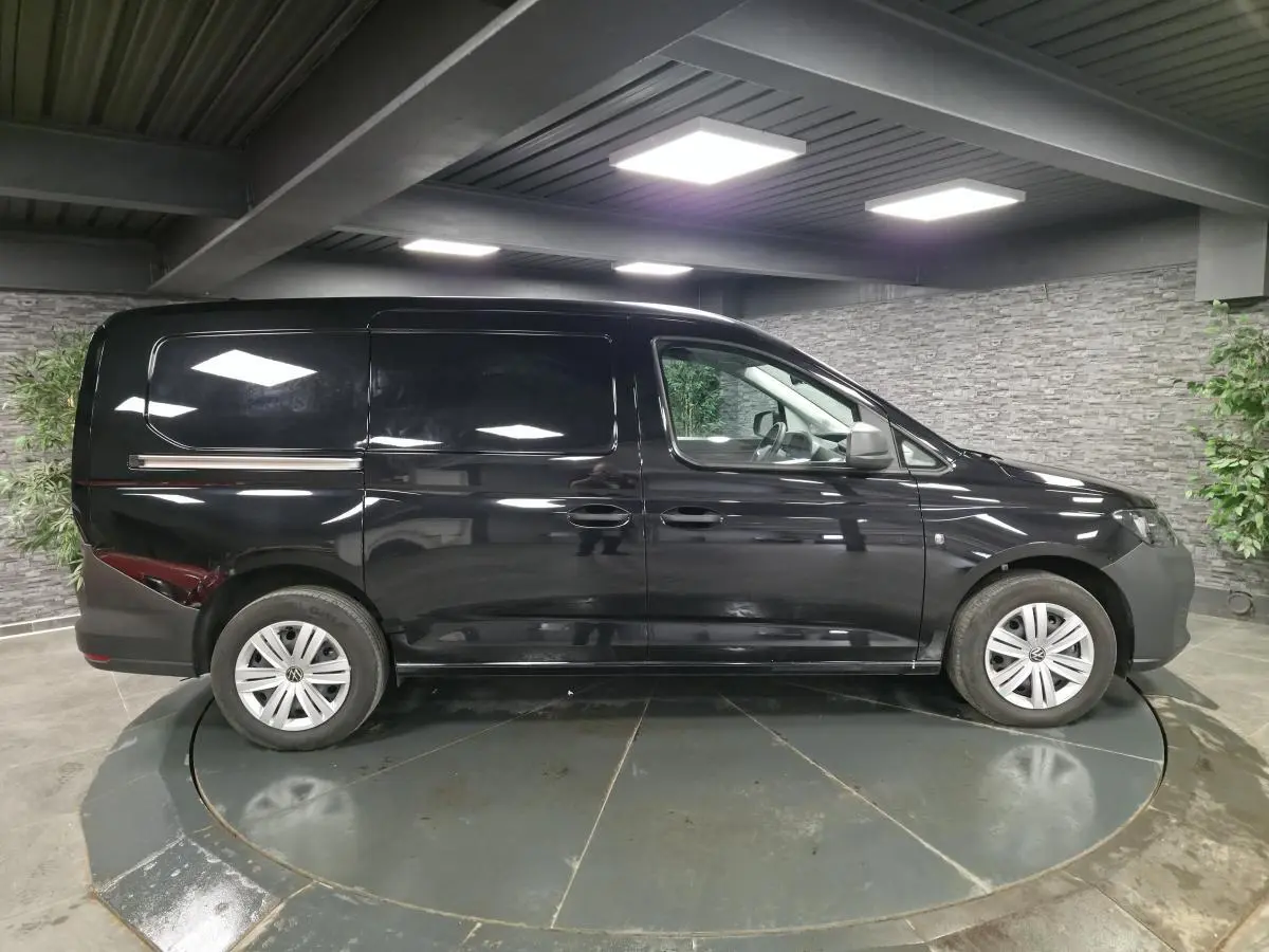 Vue latérale droite d'un Volkswagen Caddy Cargo noir 2024 avec jantes acier et porte coulissante tôlée.