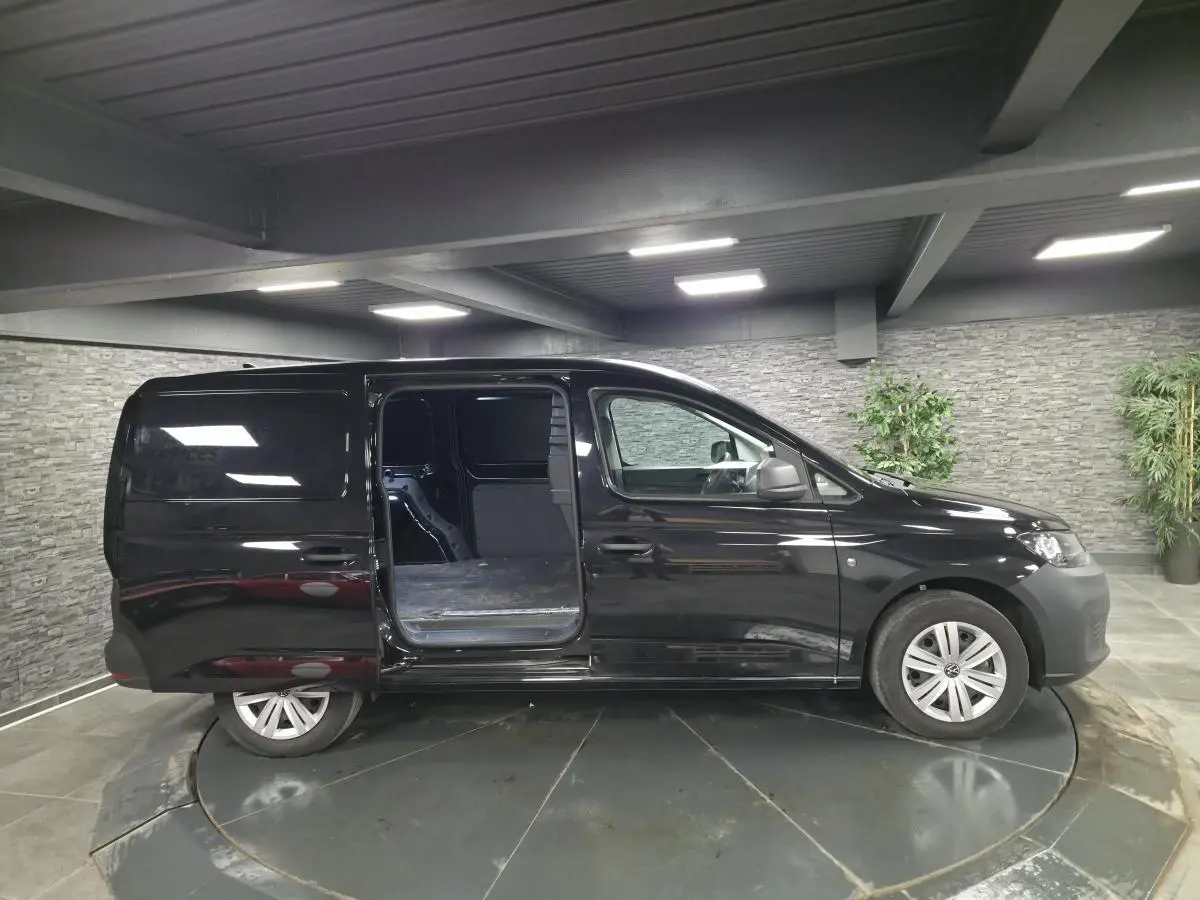 Vue latérale droite d'un Volkswagen Caddy Cargo noir 2024 avec porte coulissante ouverte en intérieur.
