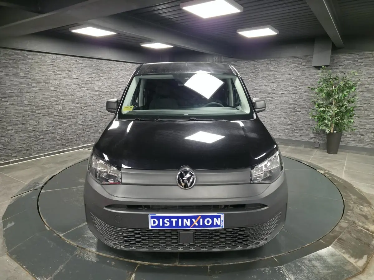 Vue de face d'un Volkswagen Caddy Cargo 2024 noir avec pare-chocs gris et calandre inférieure à motif nid d'abeille.