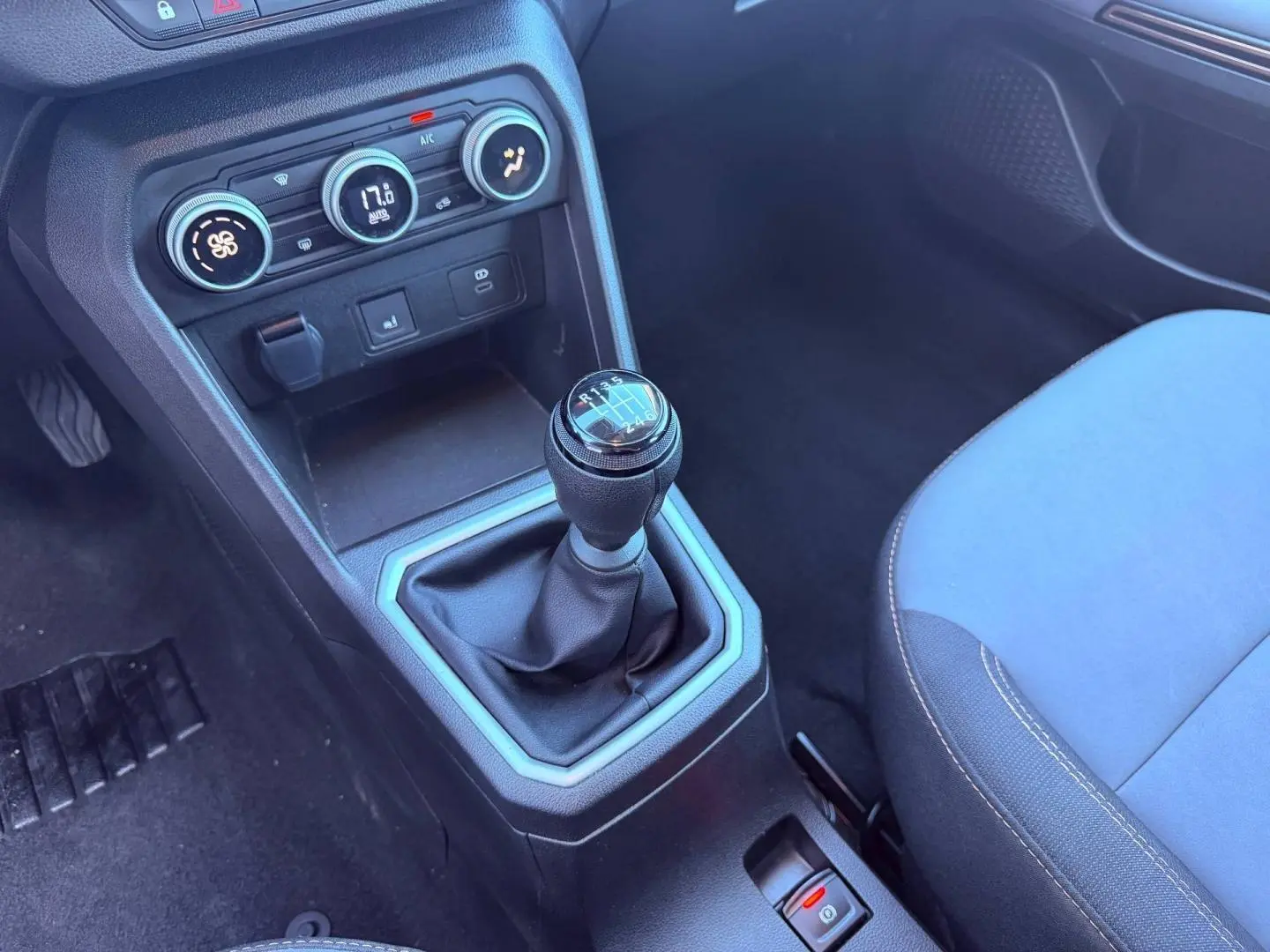 Gros plan sur la console centrale de la Dacia Sandero 2025, avec levier de vitesses manuel et sièges tissu bleu.