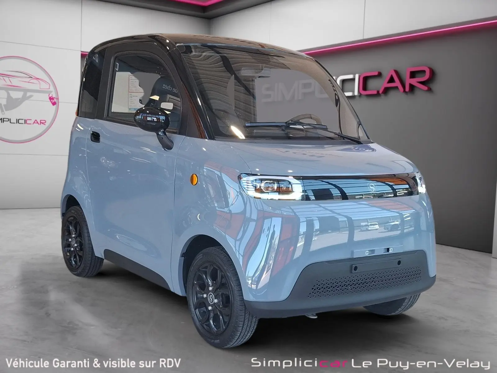 Vue 3/4 avant gauche de la Simplici S1 électrique gris perle avec toit noir et jantes noires en intérieur showroom.