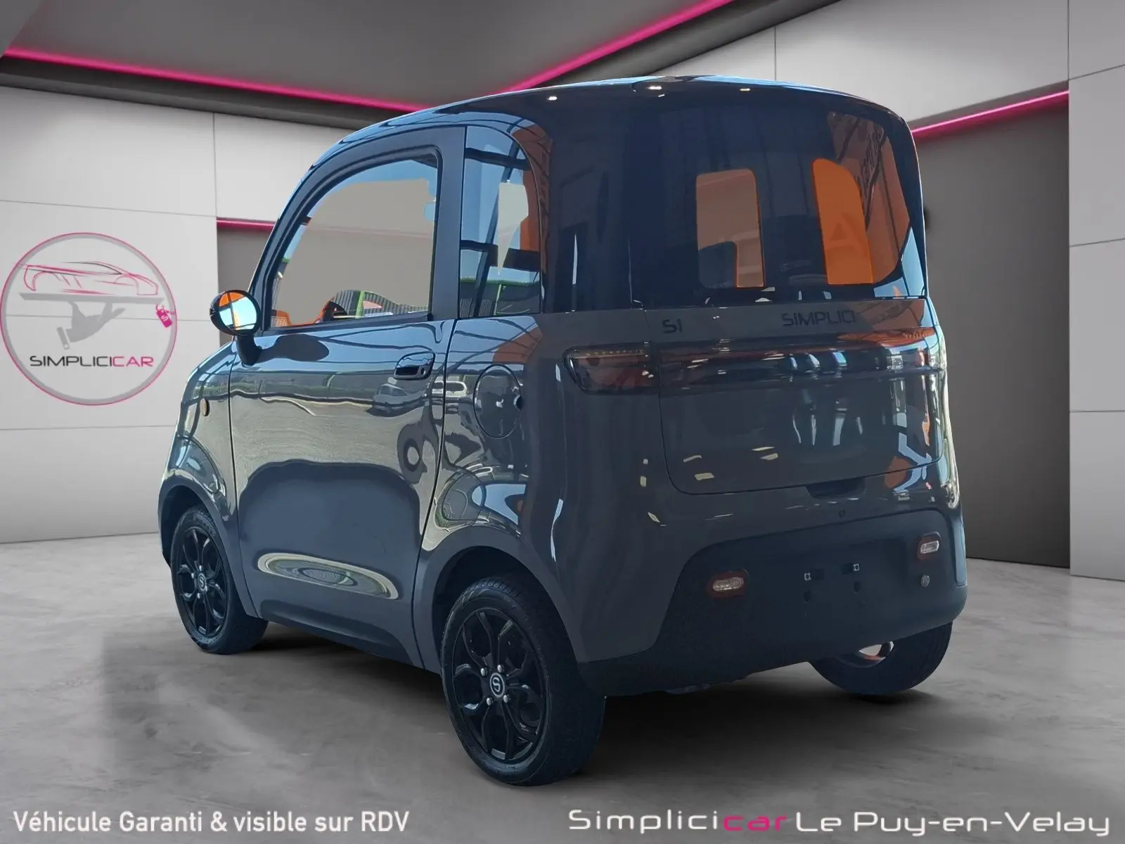 Vue 3/4 arrière droite de la SIMPLICI S1 électrique 2025 gris perle avec toit noir et jantes noires en intérieur showroom.