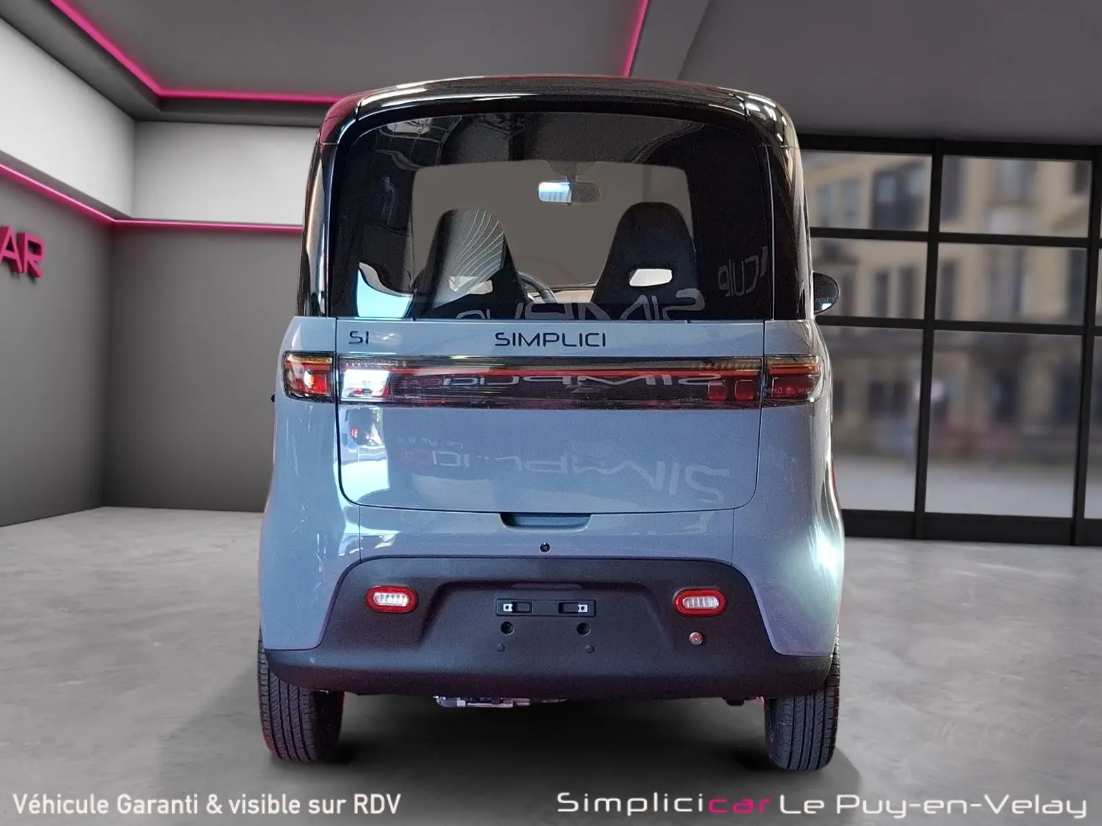 Vue arrière du Simplici S1 2025 gris perle avec toit noir, feux horizontaux et pare-chocs noir mat dans un showroom.