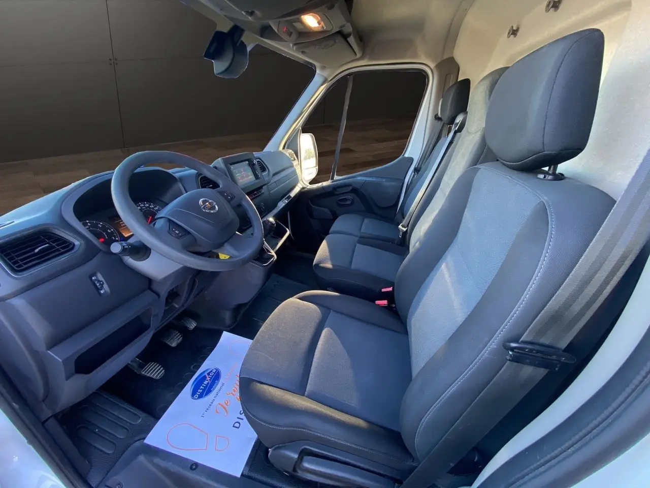 Vue intérieure côté conducteur du Nissan Interstar blanc 2022, montrant les sièges tissu et le tableau de bord avec volant.