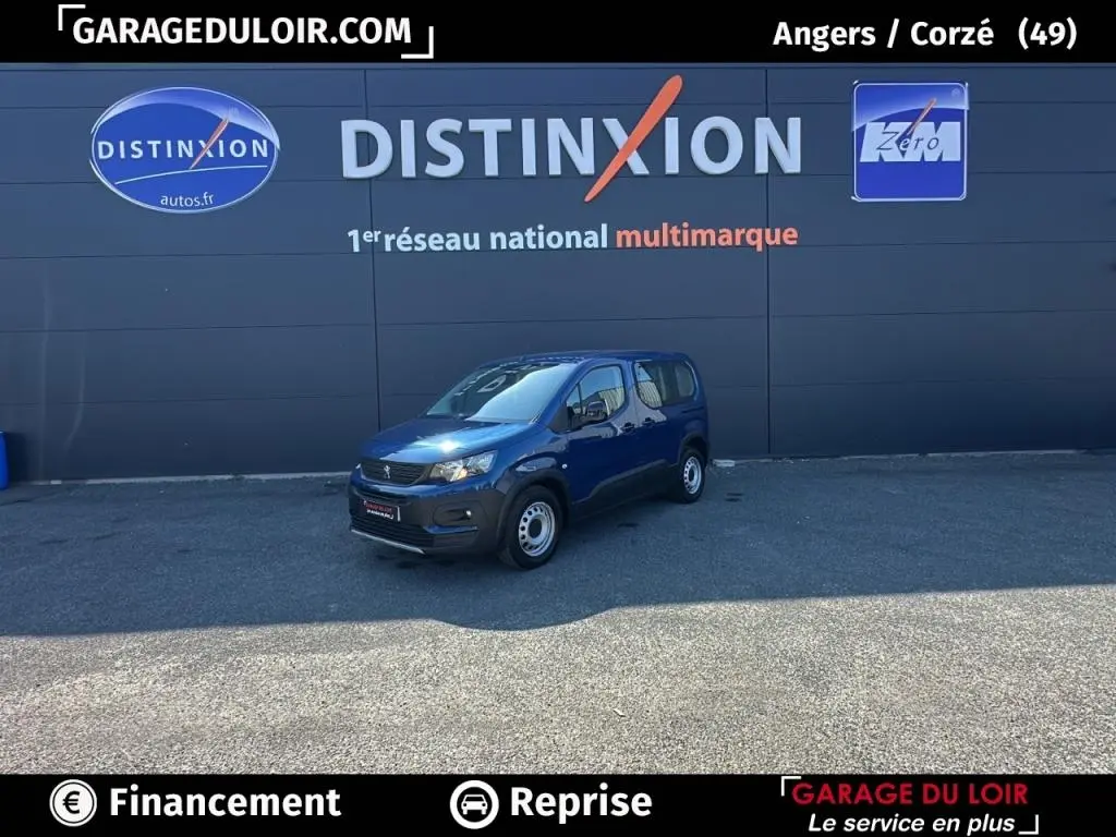 Peugeot Rifter 1.5 BlueHDi 100 Allure bleu, vue 3/4 avant droit sur parking devant mur gris avec logo Distinxion.