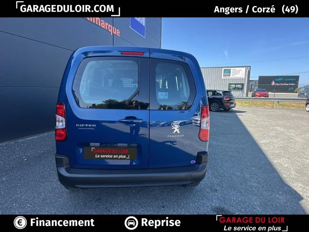 Vue arrière d'un Peugeot Rifter bleu 2024 avec portes battantes et logo Peugeot visible, stationné en extérieur.