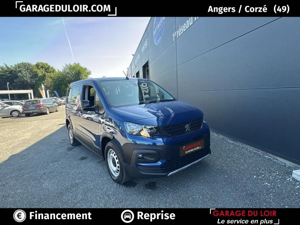 Peugeot Rifter bleu 2024 en 3/4 avant droit, finition Allure, garé devant un bâtiment gris industriel.