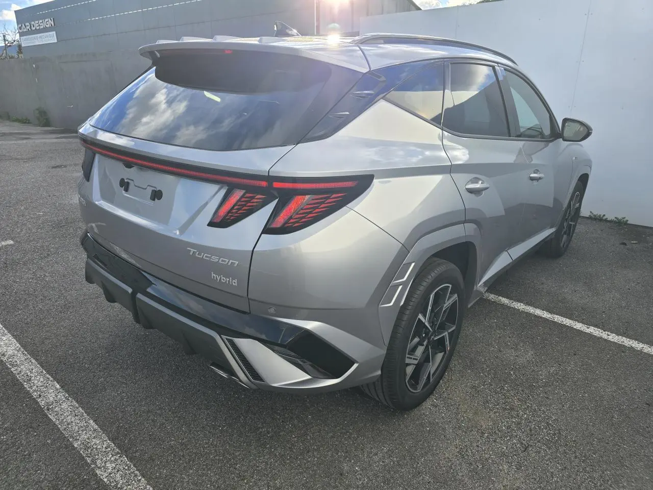 Vue 3/4 arrière droite du Hyundai Tucson 2025 hybride en argent métallisé avec feux arrière LED et jantes alliage noires.