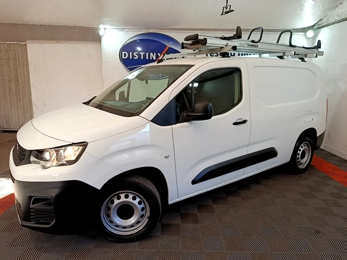 Vue 3/4 avant droite du Peugeot Partner blanc avec galerie de toit et jantes acier en intérieur fermé.