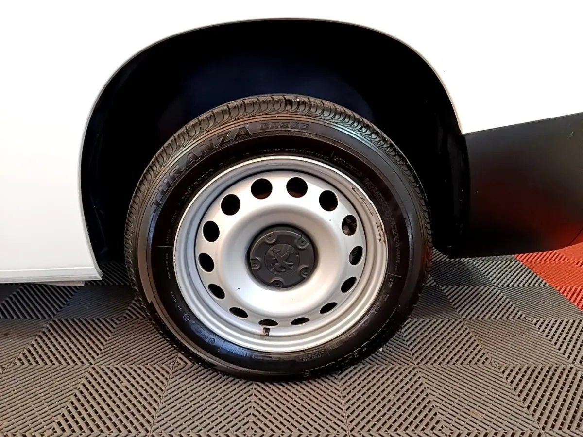 Gros plan sur la roue arrière droite en jante acier du Peugeot Partner blanc, avec partie basse de la carrosserie visible.