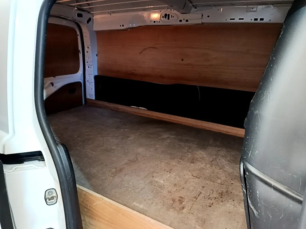 Vue intérieure du compartiment de chargement du Peugeot Partner blanc, montrant le revêtement bois et la cloison pleine arrière.