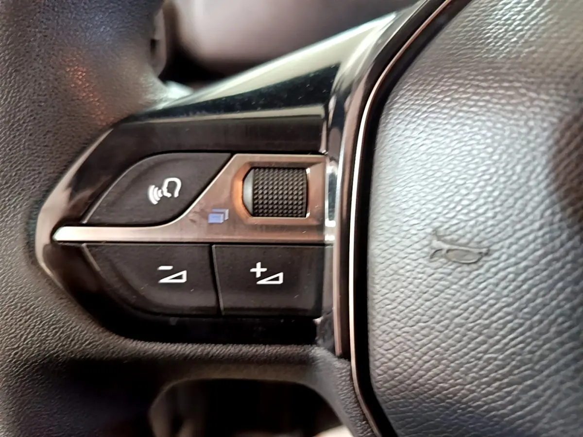Gros plan sur les commandes de volume et de reconnaissance vocale sur le volant noir du Peugeot Partner blanc.