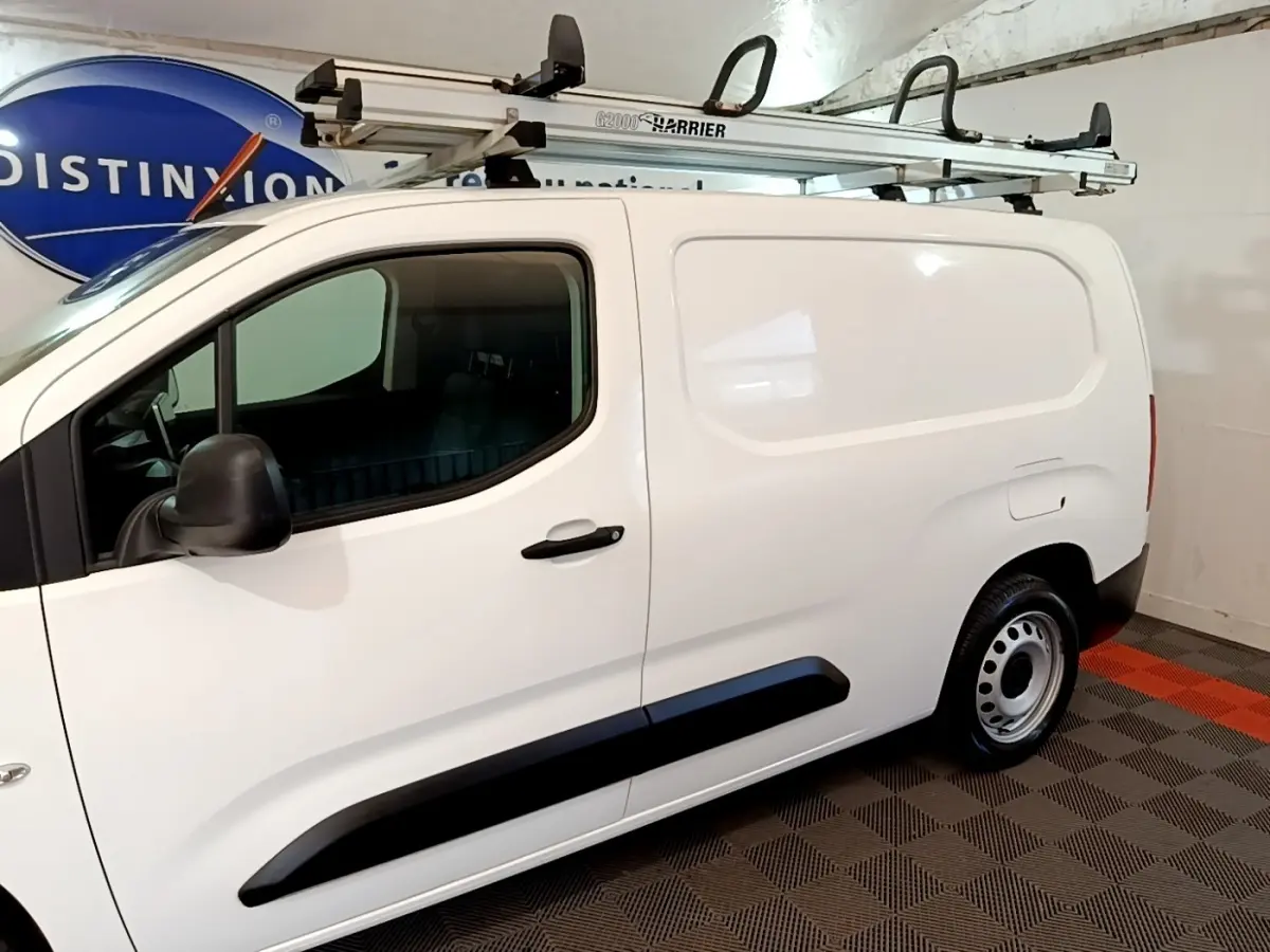 Vue latérale droite d’un Peugeot Partner blanc utilitaire avec galerie de toit et jantes acier en intérieur.