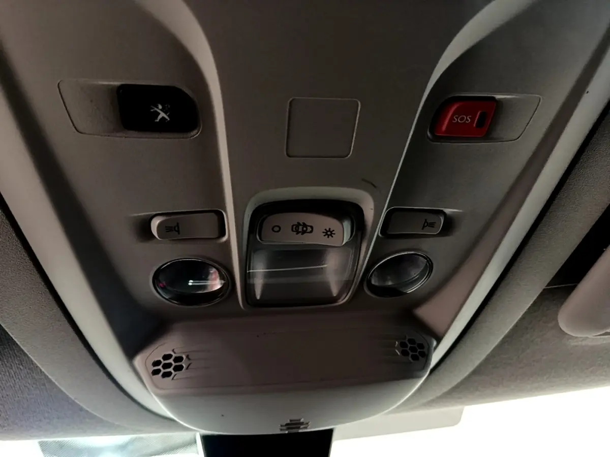 Vue intérieure en contre-plongée du plafonnier gris avec boutons d’éclairage et bouton d’appel d’urgence rouge dans un Peugeot Partner blanc.
