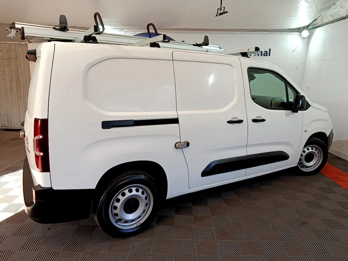 Vue côté droit d'un utilitaire Peugeot Partner blanc avec galerie de toit et jantes acier en intérieur fermé.