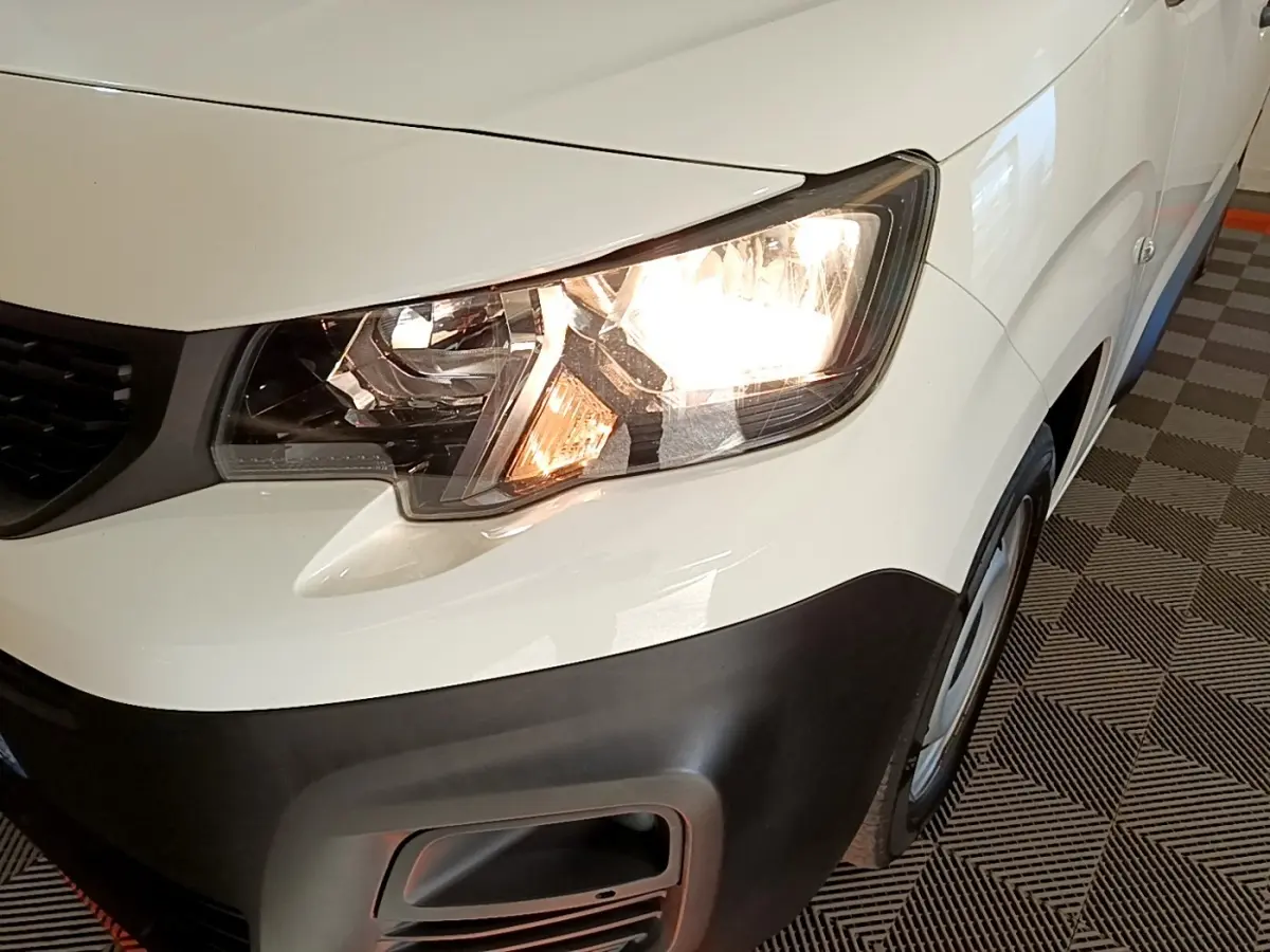 Gros plan sur l'avant droit blanc du Peugeot Partner 2021 avec phare allumé et pare-chocs noir mat.