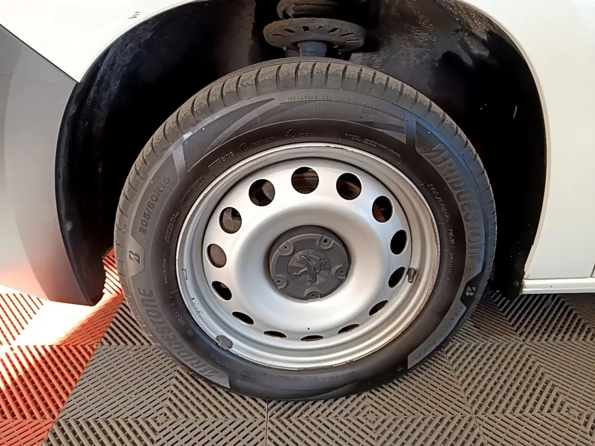 Gros plan sur la roue avant droite blanche d’un Peugeot Partner 2021 avec jante acier et logo Peugeot central.