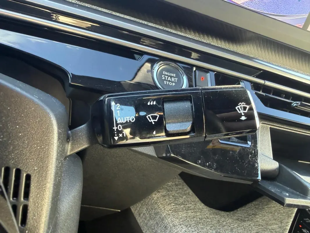 Gros plan sur la commande d’essuie-glace noir brillant et le bouton start/stop du tableau de bord gris du Peugeot 3008 Hybrid 2025.