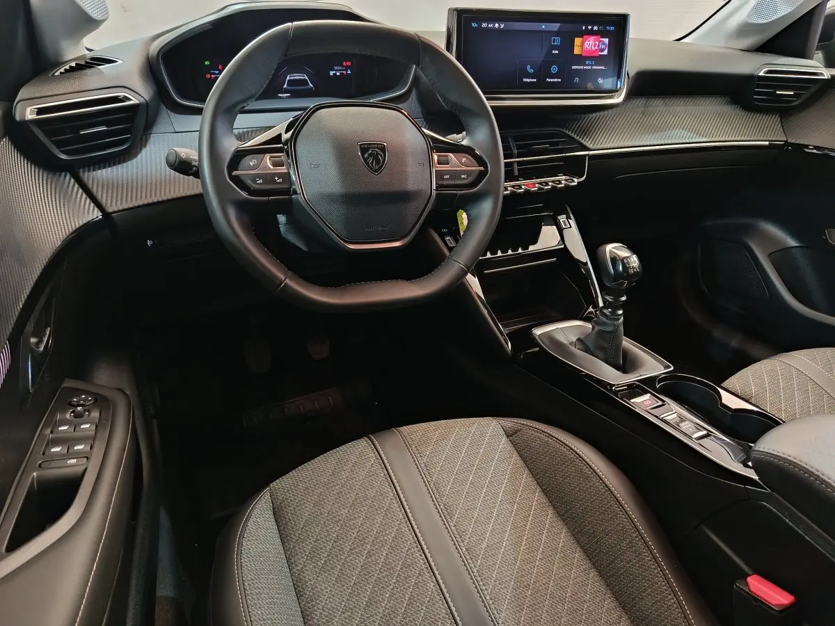 Intérieur noir de la Peugeot 208 PureTech 100 S&S Allure, vue centrée sur le volant et la console avec boîte manuelle.